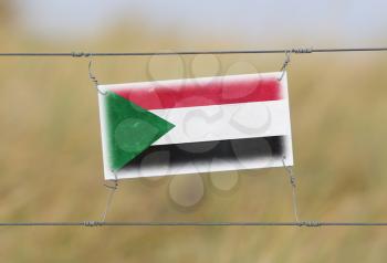 Border fence - Old plastic sign with a flag - Sudan