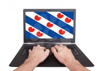 Hands working on laptop showing on the screen the flag of Friesland