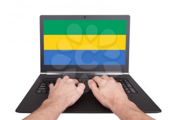 Hands working on laptop showing on the screen the flag of Gabon