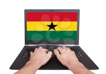 Hands working on laptop showing on the screen the flag of Ghana
