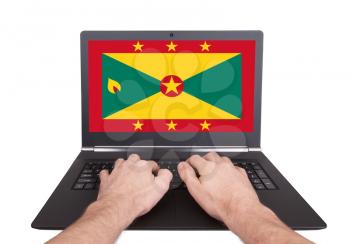 Hands working on laptop showing on the screen the flag of Grenada