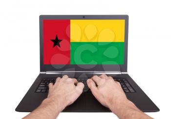Hands working on laptop showing on the screen the flag of Guinea-Bissau