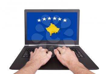 Hands working on laptop showing on the screen the flag of Kosovo