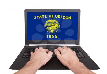 Hands working on laptop showing on the screen the flag of Oregon