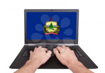 Hands working on laptop showing on the screen the flag of Vermont