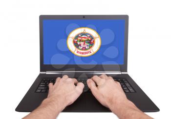 Hands working on laptop showing on the screen the flag of Minnesota