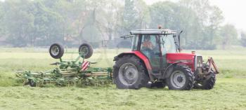 Leeuwarden, the Netherlands - May 26, 2016: Farmer uses tractor to spread hay on a field in Friesland, the Netherlands on May 26, 2016.