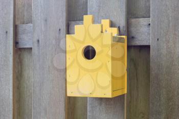 Yellow birdhouse on a wooden fence in a garden
