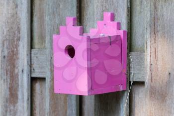 Pink birdhouse on a wooden fence in a garden