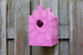 Pink birdhouse on a wooden fence in a garden