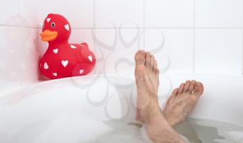 Men's feet in a bathtub, with large rubber duck, selective focus
