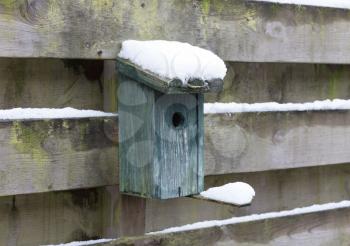 Birdhouse covert in snow, hanging on a wooden fence