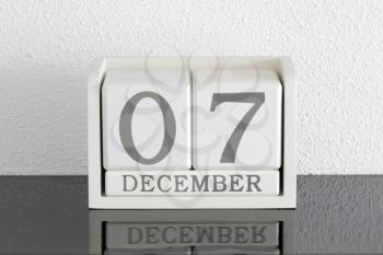 White block calendar present date 7 and month December on white wall background