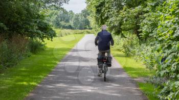 Unrecognisable old man riding a bike on asphalt road