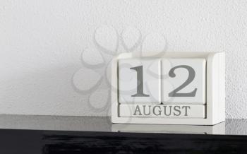 White block calendar present date 12 and month August on white wall background