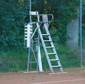 Old tennis umpire chair on a red tennis court
