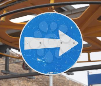 Blue road sign with white arrow pointing right, ski lift in Switzerland
