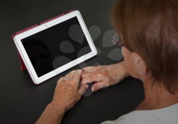 Senior lady relaxing and reading the screen of her tablet, black screen visible