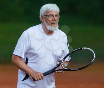 Senior man playing tennis on a gravel court