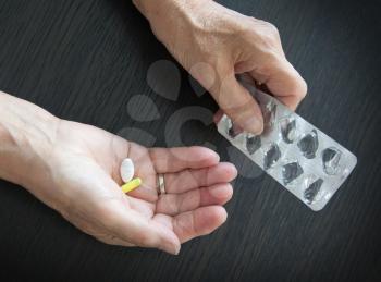 Elderly person taking medication, two different pills