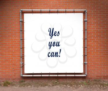 Large banner with inspirational quote on a brick wall - Yes you can!