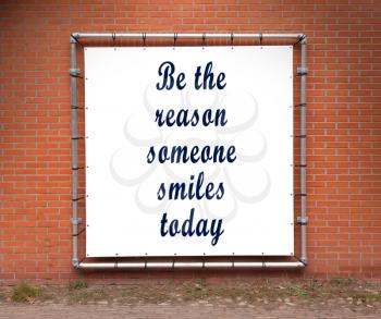 Large banner with inspirational quote on a brick wall - Be the reason someone smiles today