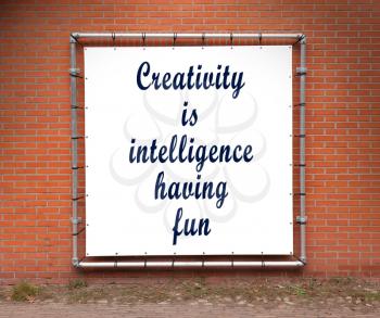 Large banner with inspirational quote on a brick wall - Creativity is intelligence having fun