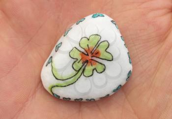 Stone with drawing of a clover four and small hearts, isolated on a hand