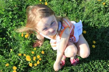 little fashionable girl lying on the green grass with dandelions