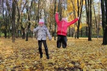two little girls jumping in the park with yellow leaves