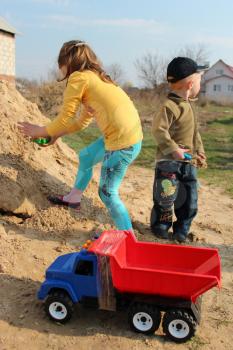 little girl and boy playing in the sand-box with toys