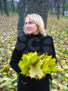 The beautiful woman with yellow leaves at a tree in the autumn