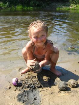 little girl is playing on the sand of the river