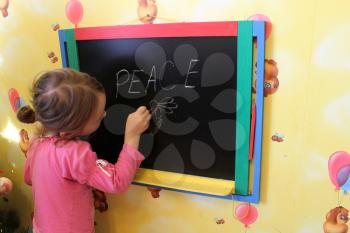 little girl writes on blackboard word Peace
