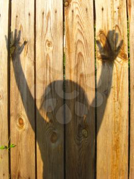 shadows of teen's hand raising up on the wooden fence
