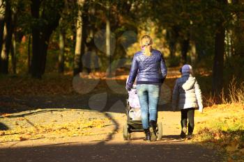woman with baby in perambulator and elder child walking in the autumn park