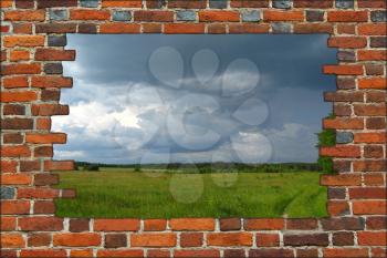 broken brick wall and view to field with dark thunder storm clouds