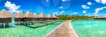 Panorama of Water Villas (Bungalows) and wooden bridge at Tropical beach in the Maldives at summer day