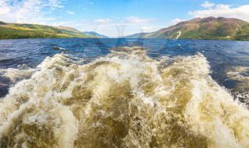 Trail on water surface behind motor boat on Loch Ness in Scotland in a beautiful summer day, United Kingdom