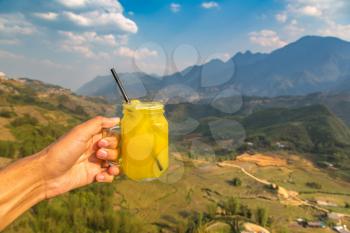 Hand with a glass of pineapple juice in front of Terraced rice field in Sapa, Vietnam in a summer day