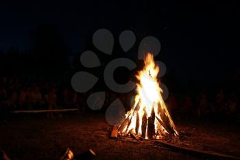 Blurred People sit at night around a bright bonfire