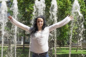 Caucasian brunette woman with upward hands on fountain background