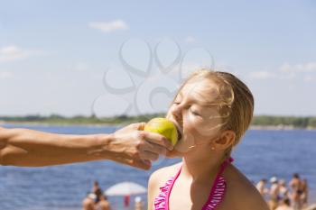 Photo of girl biting an apple from mother hand