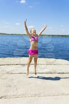 Jumping girl on the riverbank in pink swimsuit