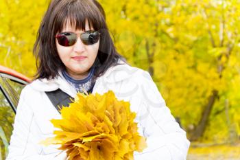 Beautiful brunette in yellow autumn with bouquet of sheets