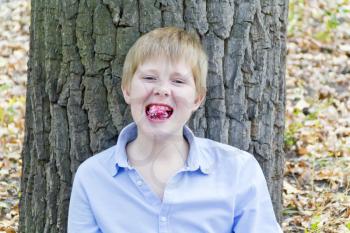 Boy sitting near tree and eating dessert with appetite