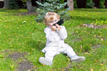 Cute baby girl with mobile phone sitting on green grass