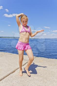 Dancing girl in pink swimsuit on the riverbank 