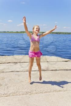Cute jumping girl on the riverbank in pink swimsuit