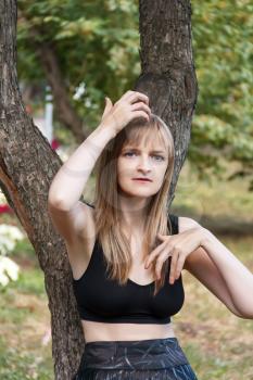 Blond woman correcting hairstyle near tree in summer